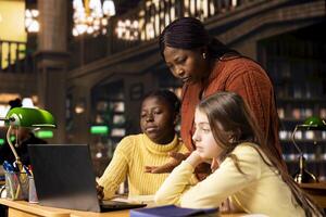 Two elementary school children working with a tutor practicing mathematics and developing their academic skills at a study desk. Black woman explains the curriculum materials to her pupils. photo