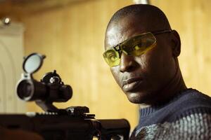 Portrait of man in shooting gallery training, learning proper semiautomatic weapons handling. Person practicing with rifle, wearing safety goggles to prevent debris from getting in eyes, close up photo