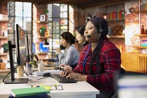 Call center agent in office talking in headset mic, communicating with customer, providing step by step guidance. Woman does customer support job at PC desk walking clients through technical solutions photo