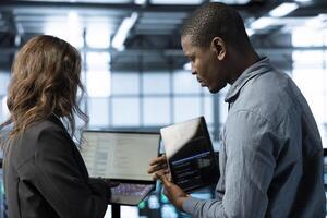 System administrators in data center using laptop and tablet, integrating green technologies. IT specialists in server room using devices to implement sustainable energy solutions photo