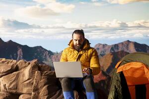 Young explorer keeps working at the top of the mountain with internet everywhere, enjoying global connectivity and productivity on the hill summit. High speed strong signal on a hike. photo