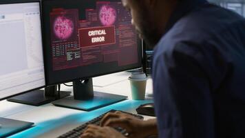 Programmer seeing red critical error popup on computer display in data center, panicking. African american man in server hub spamming keyboard buttons after receiving error, camera A photo