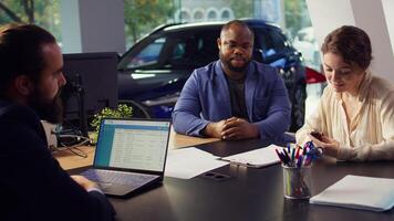 Panning shot of car dealership table with salesman and clients sitting and talking after finishing test drive. Agent discussing with couple wanting to lease vehicle, camera B close up photo