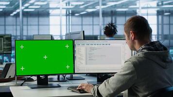 Software developer using green screen PC to do programming in server room providing computing resources for workloads. IT expert supervising data center supercomputers using mockup computer, camera A photo