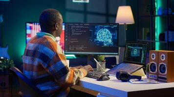 Professional male developer manages neural network at desk, working with AI code on laptop. African american IT expert freelancer developing cyber security, creating secure database. Camera A. photo