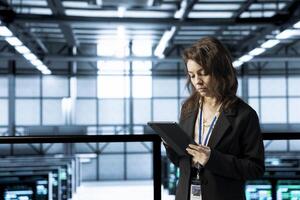 System administrator in data center uses automation tools on tablet, running predictive maintenance routines. IT expert ensuring continuous uptime of server farm, managing data flows with device photo