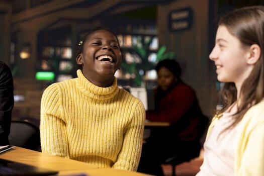 Adorable girlfriends gossiping and joking around in the school library, taking a break from class assignment and enjoying team project with each other. Young girls enjoying a conversation. photo