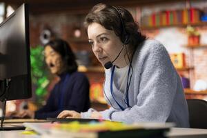 Call center employee using headset microphone to answer customers technical inquiries, assisting with questions about hardware issue. Woman doing customer service job using PC to troubleshoot problems photo