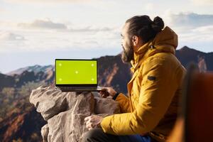Young traveler embraces high altitude wilderness next to chroma key, using a device where the crisp air and scenic mountain view provide an inspiring setting for trekking and adventure. photo
