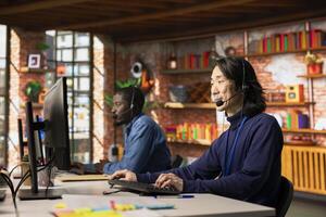 Team of customer service staff members tracking support ticket in dedicated company software on PC. Asian call center worker and african american colleague talking with customer calling photo