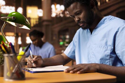 African american medical student creates a summary of class notes to learn easily for an exam, collecting information from the library to complete his knowledge. Future doctor at desk. photo