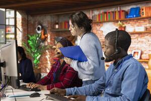 Call center team leader supervising agents at office desk handling customer inquiries, complaints and support requests. Customer service manager overseeing workers assisting clients photo
