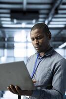 Engineer in data center using laptop, adjusting power management settings, verifying compliance requirements, optimizing resource utilization, maintaining stable infrastructure photo