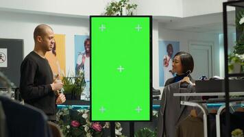 Asian retail worker recommends new designer items next to chroma key screen, suggesting colorful clothes for middle eastern man. Female assistant helping client with wardrobe essentials. photo
