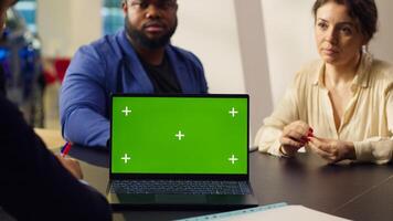 Customers in showroom looking for new vehicle to purchase, being shown options by salesman on mockup laptop. Agent using green screen notebook to help clients evaluate cars, camera A photo