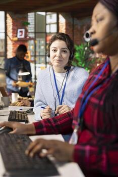 Portrait of smiling call center onboarding specialist providing training to new recruit on PC. Friendly manager in customer support workspace providing support on how to use company platforms photo