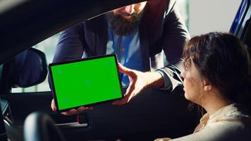 Showroom salesman showing car brochure and price list on green screen tablet to clients after they finished test drive. Dealership agent showing vehicle catalog to customers on mockup device, camera A photo
