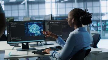 Engineer waiting at PC desk for checkup to be done on AI server room providing computing resources. African american woman investigating data center mainframes using computer, camera A photo