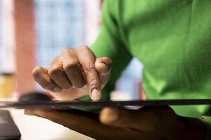 Remote employee at home office desk editing documents on tablet, updating reports and files. Close up of teleworker managing digital documents on device, typing on touchscreen display photo