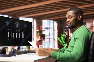 Upbeat teleworker using financial software user interface on PC screen in apartment showing company growth graphs. Man looking at sales statistics on computer display showing income figures photo
