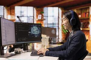 CTO manager in artificial intelligence focused startup designing and debugging applications, listening music. Asian technician wearing headphones doing code testing and quality assurance photo