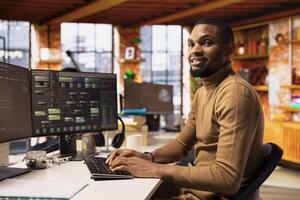 Portrait of smiling IT expert using PC in startup office to design and implementing algorithms enabling machine learning. African american tech venture employee conducts code reviews to fix bugs photo
