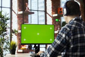 Man wearing headphones engaging in online training session on green screen PC, navigating course modules, watching instructional videos, completing quizzes, noting key concepts photo