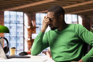 Man at home feeling exhausted and in pain from lack of sleep, suffering from insomnia fatigue. Exhausted African american person with negative emotion affected by ache, closing eyes, feeling stressed photo