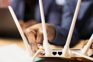 Young black woman pulling out the LAN cable from the modem while her boyfriend reads a technical manual on laptop for troubleshooting. Wi-Fi reset to fix connectivity issues. Close up. photo