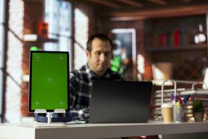 Man in home office uses isolated screen tablet, preparing presentation slides, adjusting layouts. Employee finishing company project, writing summaries, saving files on chroma key device photo