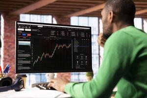 Day trader using computer, purchasing stocks that might perform well and selling ones that might drop in value. Forex trader browsing though stock exchange portfolio pages at PC desk photo