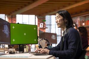 Senior programmer using chroma key computer to oversee artificial intelligence neural networks. Tech startup experienced IT worker using AI systems on green screen PC display photo