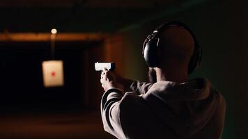 Person wearing protecting gear loading magazine in pistol during firearm practice session at shooting range. Gun enthusiast reloading handgun, learning self defense, pointing weapon, camera B photo