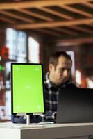Focus on green screen tablet used by man in blurry background using mockup device, composing social media posts. Close up of chroma key tablet used by employee to monitor company social media photo