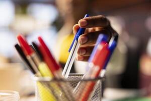 Extreme close up of pen taken by person from desk organizer to annotate document. Focus on workspace stationary holder used by student in blurry background requiring writing tool photo