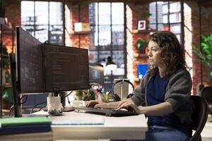 IT specialist at workstation programming on monitor and writing lines of code, using development tools and a terminal window interface. Woman debugging software before deadline. photo