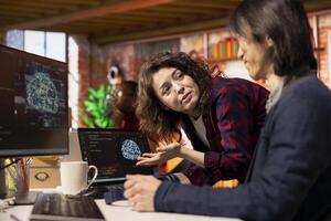 Startup intern asks questions to senior technician coding advanced AI algorithm and machine learning models enhancing automation. Employee requests help from CTO manager in Silicon Valley workplace photo