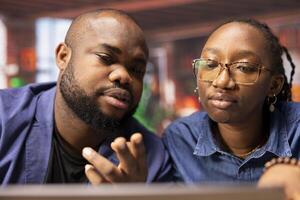 African american couple working remotely in their apartment, planning business strategies and discussing project development while using a laptop to track progress and ensure success. photo