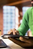 Man in living room using tablet to compose social media posts, producing content. Close up of african american person monitoring social media engagement using digital device photo