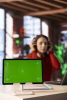 Casual person joining virtual workshop online next to chroma key screen, uses headset during the lesson on a website. Focused woman on virtual network connection, multitasking at home. photo