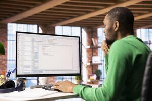 Programmer types code into PC, entering commands, running script. African american IT specialist in apartment office fixing errors in application, implementing new features photo