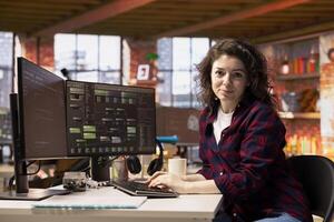 Portrait of smiling woman in startup office designing, coding and debugging applications in different software languages. Cheerful IT specialist doing code testing and quality assurance photo