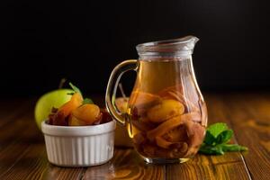 Refreshing drink in a jug with apricots, isolated on black background photo