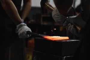Blacksmiths forging hot metal with hammer in workshop photo