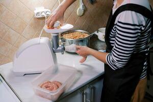 Chef stuffs the gut with minced meat on an electric meat grinder, pushing it with a pusher in the tray photo