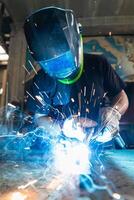 Welder in protective helmet welding metal detail in workshop photo