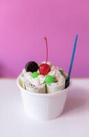 Close up of a rolled ice cream decorated with a cherry, a cookie and green bubble toppings photo