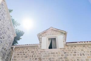 Open shutters in the attic of an old stone house against a background of sunny blue sky photo