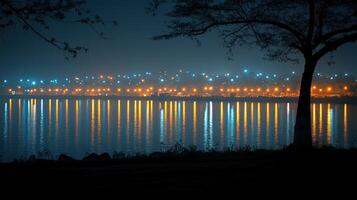 Night cityscape reflected in calm lake water, silhouetted tree. photo