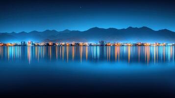 Night cityscape reflected in calm water with mountains in the background. photo